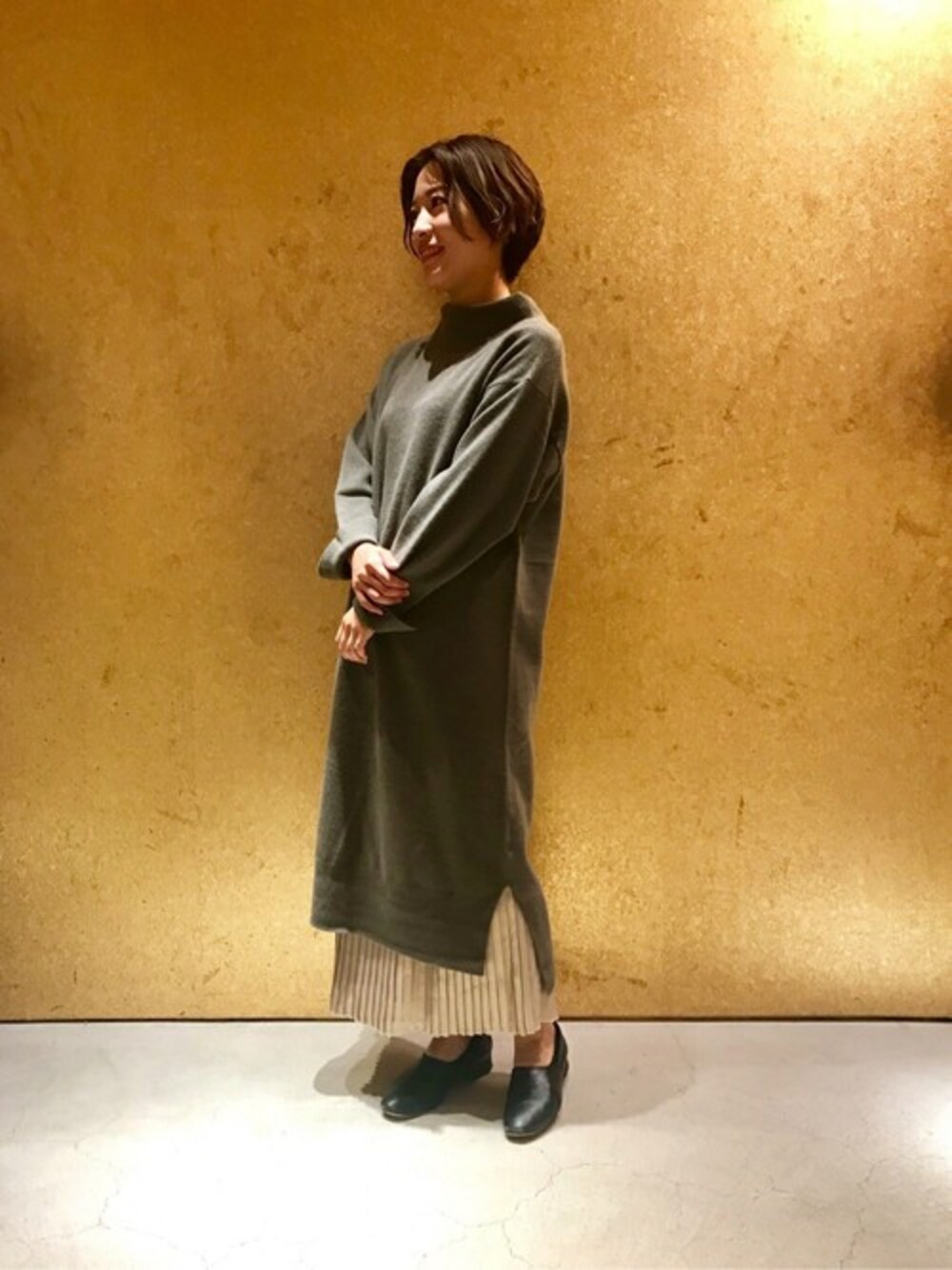 グレー系のワンピース、ゴールド系のスカートを着用したレディースの秋コーディネートの1枚目の写真