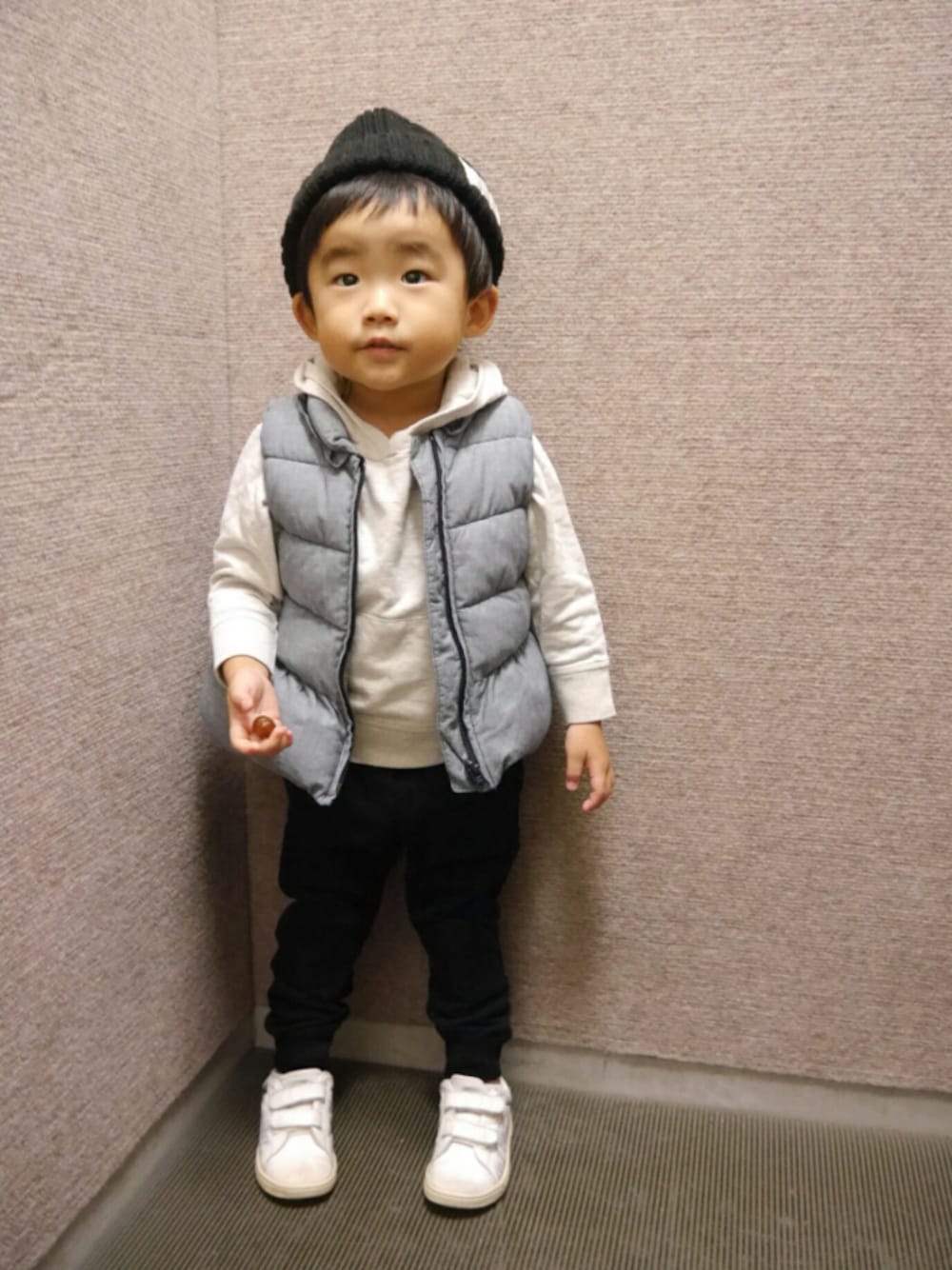 ホワイト系のスニーカー、ブラック系のパンツ、グレー系のダウンベストを着用したキッズの秋コーディネートの1枚目の写真