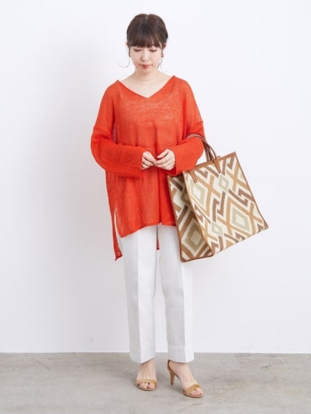 ブラウン系のバッグ、ホワイト系のデニムパンツ、オレンジ系のニット/セーターを着用したレディースの夏コーディネートの1枚目の写真