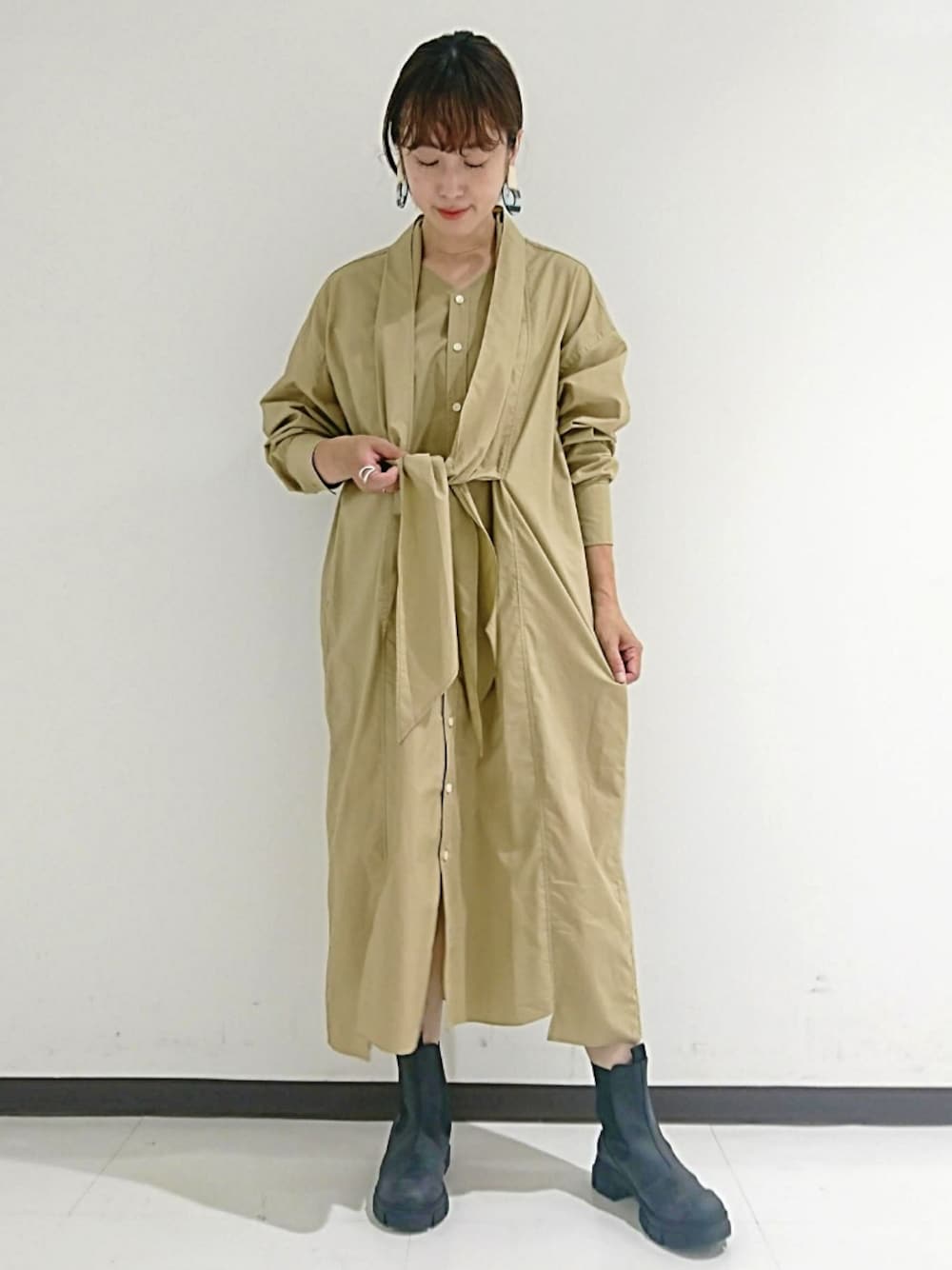 ブラック系のブーツ、ベージュ系のシャツワンピース、ブルー系のイヤリングを着用したレディースの秋コーディネートの1枚目の写真