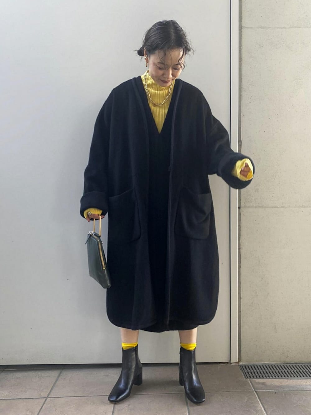 イエロー系のニット/セーター、グリーン系のハンドバッグ、ブラック系のジャンパースカートを着用したレディースの秋コーディネートの1枚目の写真