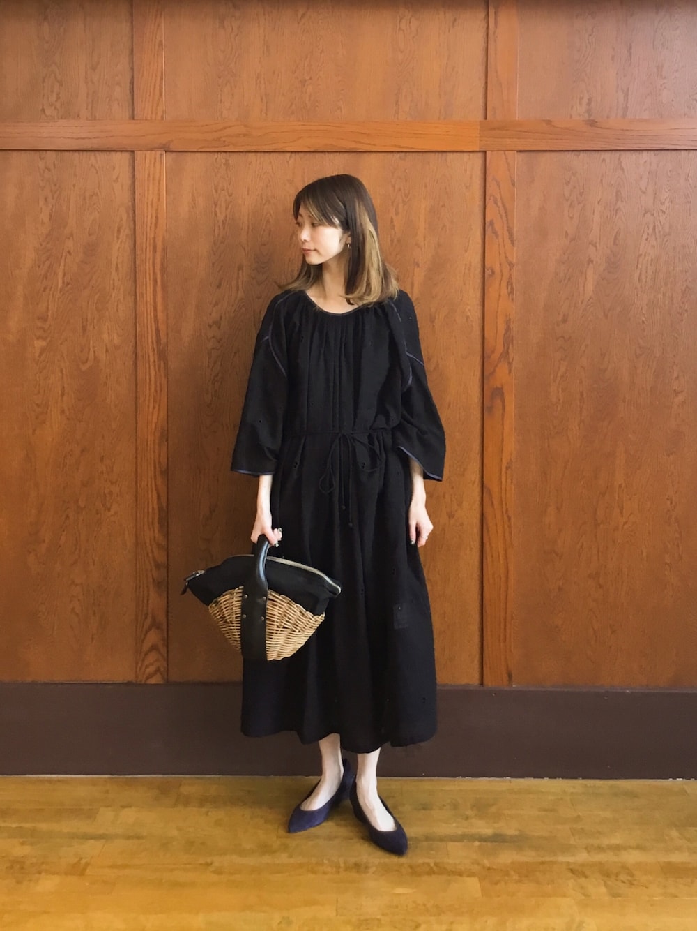 ブラック系のワンピース、ベージュ系のかごバッグ、ブルー系のパンプスを着用したレディースの冬コーディネートの1枚目の写真