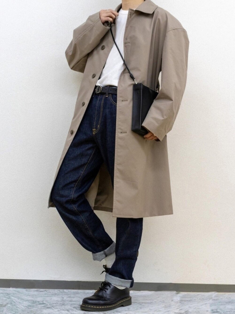 ブルー系のデニムパンツ、ブラック系のドレスシューズ、ベージュ系のステンカラーコートを着用したメンズの春コーディネートの1枚目の写真