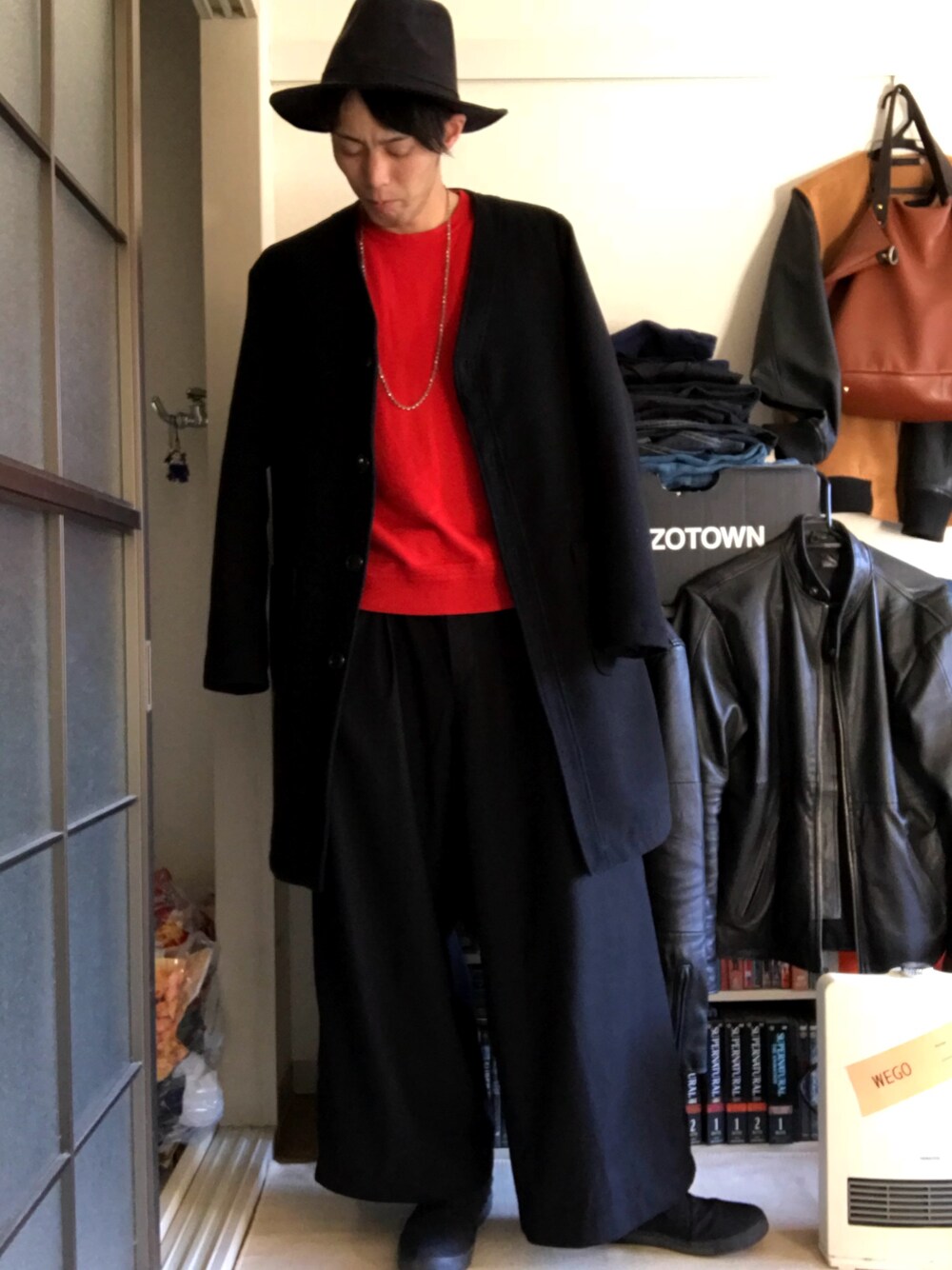 ブラック系のステンカラーコート、レッド系のニット/セーター、グレー系のスラックスを着用したメンズの冬コーディネートの1枚目の写真