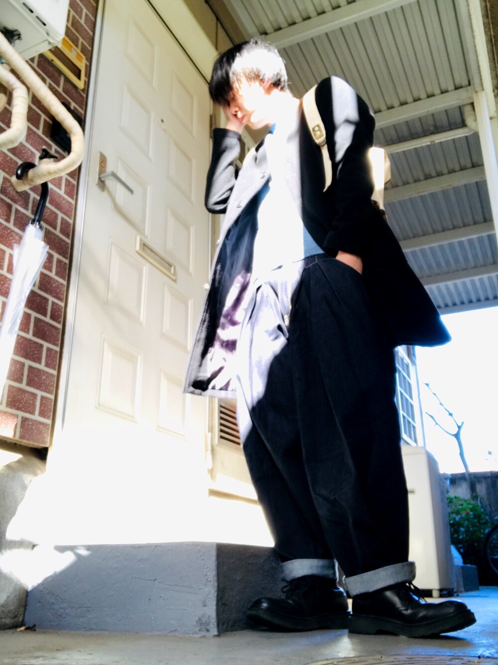 ブラック系のステンカラーコート、ブルー系のニット/セーター、ブルー系のデニムパンツを着用したメンズの冬コーディネートの1枚目の写真