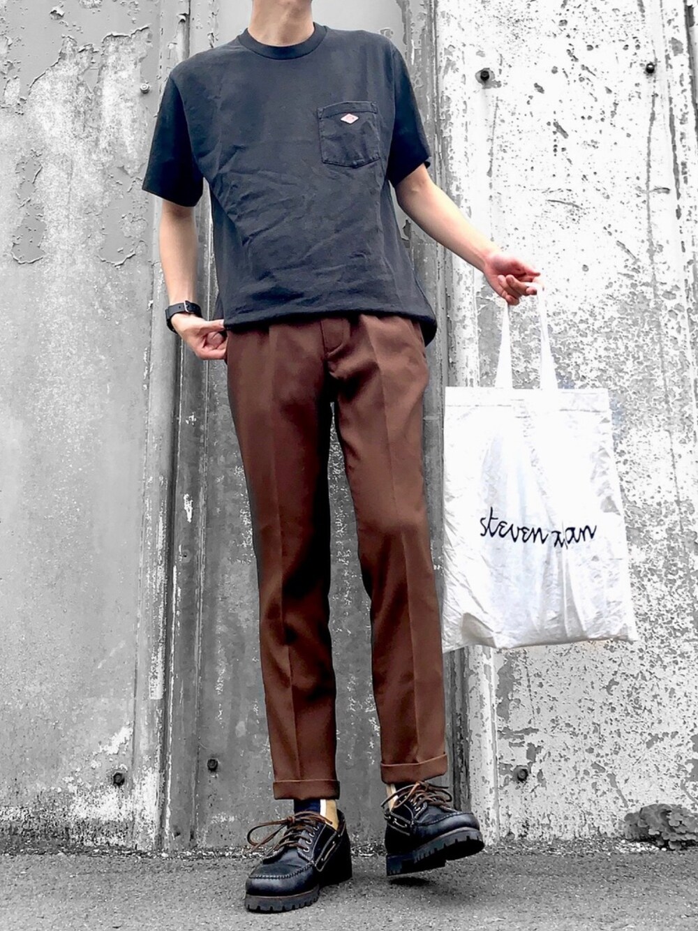 ブラック系のTシャツ/カットソー、ブラウン系のスラックス、ブラック系のモカシン/デッキシューズを着用したメンズの夏コーディネートの1枚目の写真