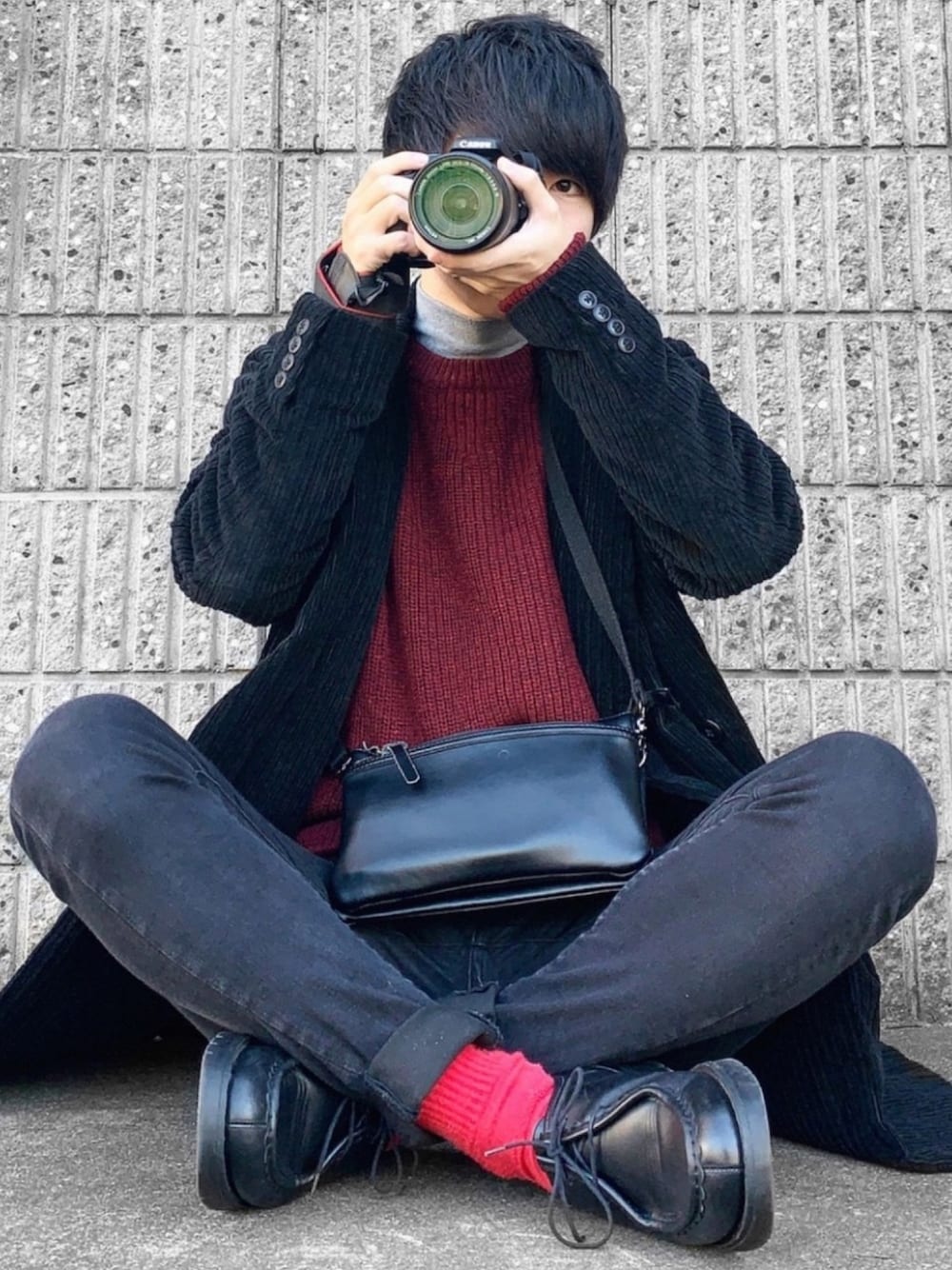 レッド系のニット/セーター、ブラック系のチェスターコート、ブラック系のデニムパンツを着用したメンズの冬コーディネートの1枚目の写真