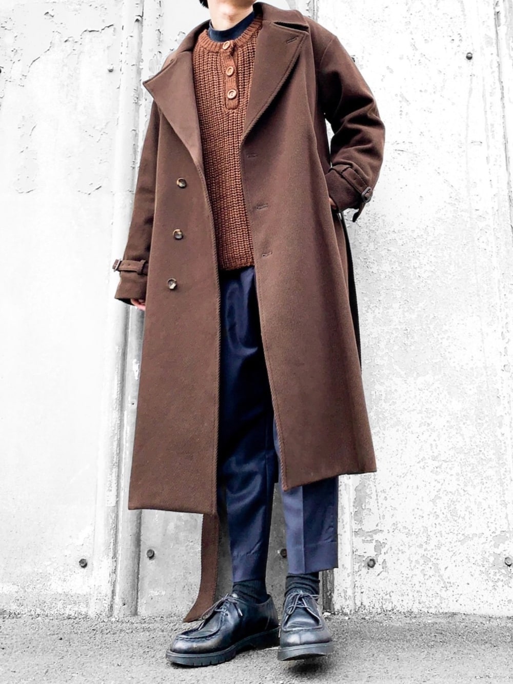 ブラウン系のチェスターコート、ブラウン系のニット/セーター、グリーン系のTシャツ/カットソーを着用したメンズの冬コーディネートの1枚目の写真