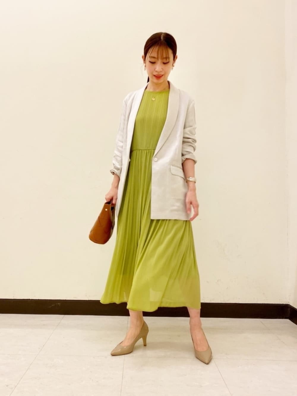 グリーン系のワンピース、ベージュ系のテーラードジャケット、ブラウン系のクラッチバッグを着用したレディースの春コーディネートの1枚目の写真