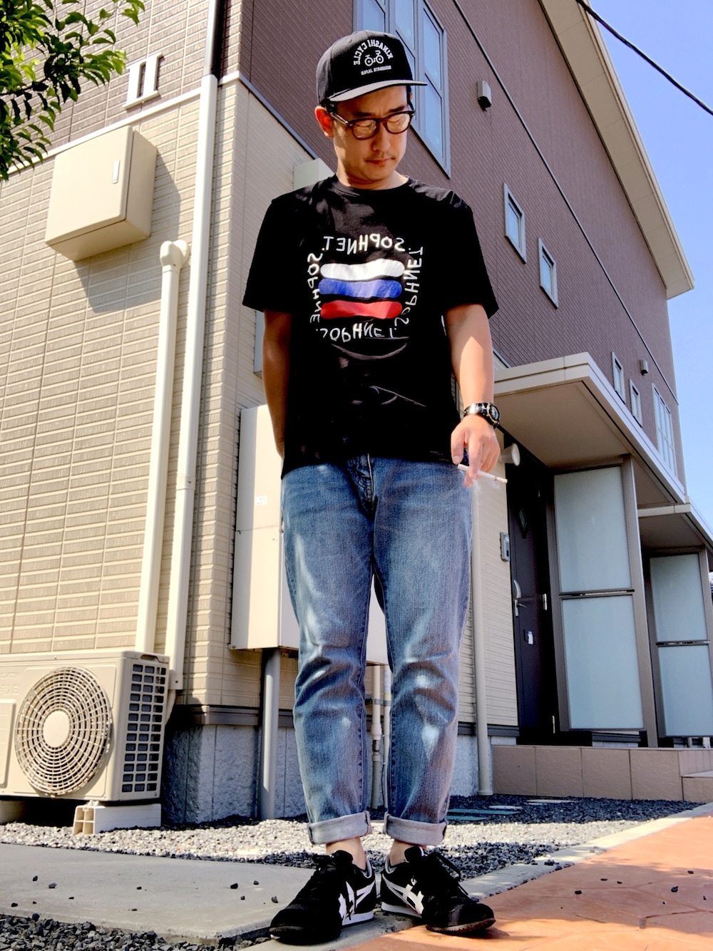 ブラック系のスニーカー、ブラック系のTシャツ/カットソー、ブルー系のデニムパンツを着用したメンズの夏コーディネートの1枚目の写真