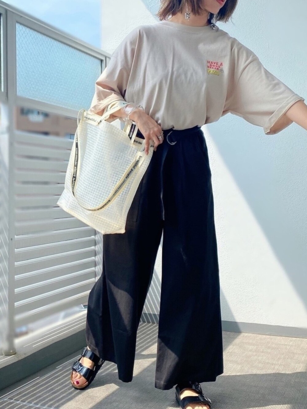 ブラック系のパンツ、ベージュ系のTシャツ/カットソー、ホワイト系のトートバッグを着用したレディースの夏コーディネートの1枚目の写真