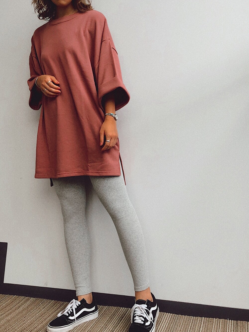 レッド系のチュニック、ブラック系のスニーカー、グレー系のレギンス/スパッツを着用したレディースの秋コーディネートの1枚目の写真