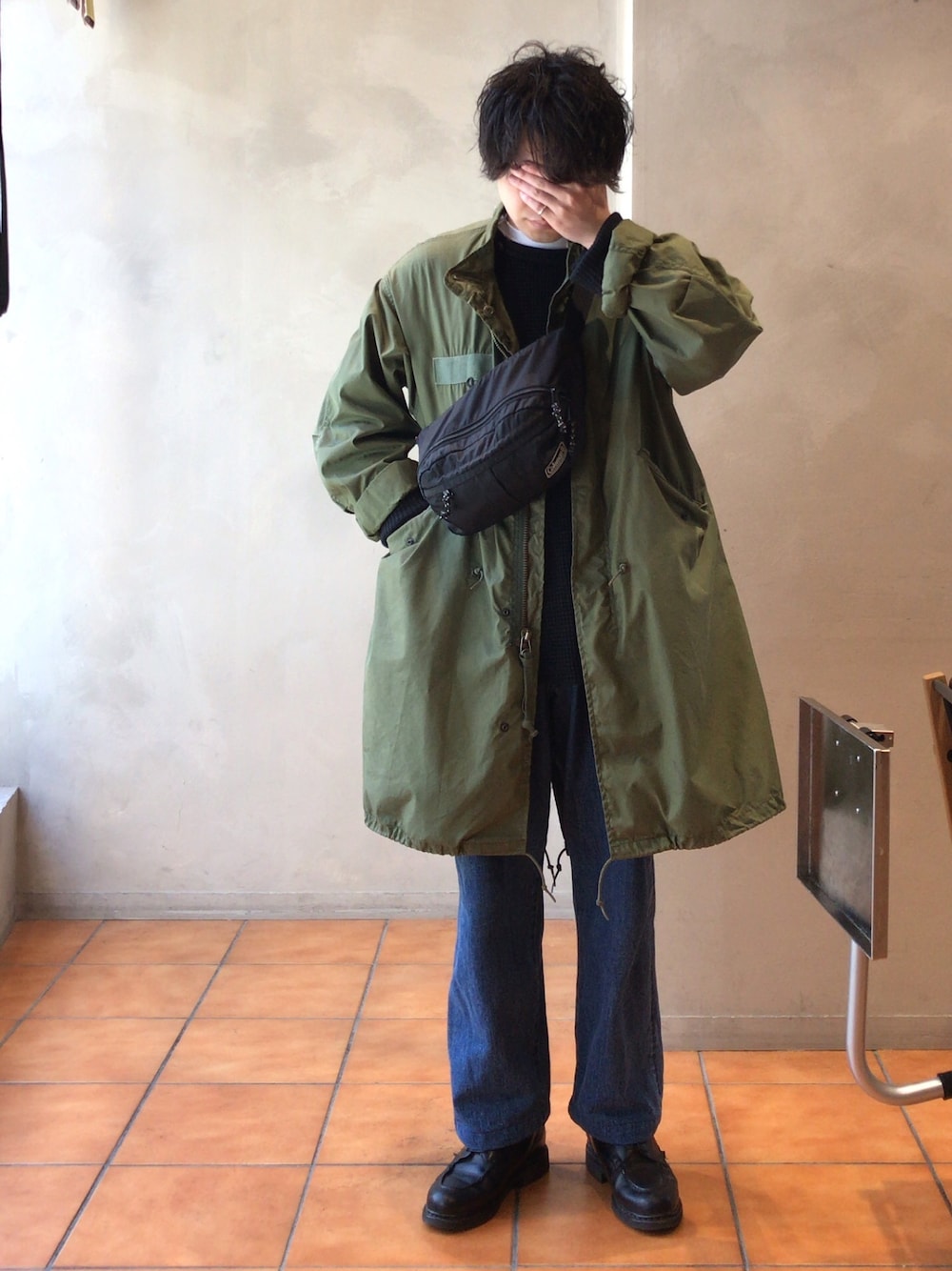 グリーン系のモッズコート、ブラック系のボディバッグ/ウエストポーチ、ブラック系のTシャツ/カットソーを着用したメンズの秋コーディネートの1枚目の写真