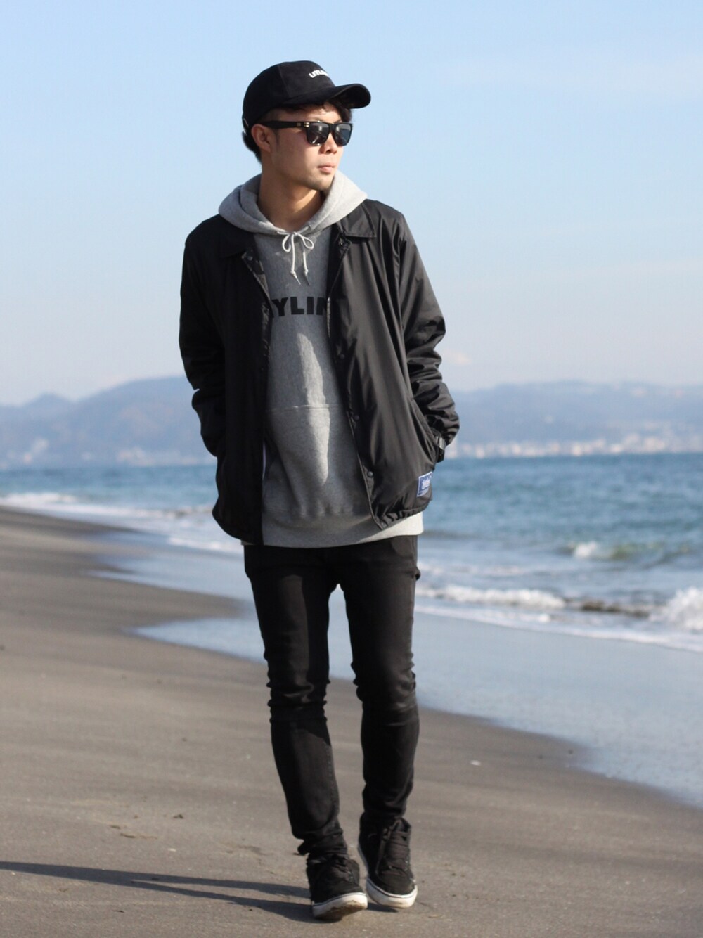 ブラック系のナイロンジャケット、グレー系のパーカー、ブラック系のキャップを着用したメンズの冬コーディネートの1枚目の写真