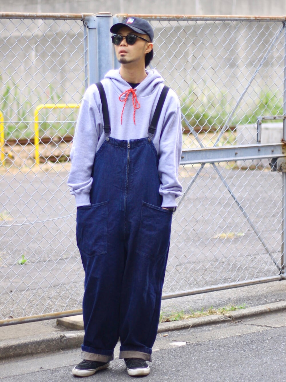 グレー系のパーカー、ブルー系のサロペット/オーバーオール、ブラック系のキャップを着用したメンズの秋コーディネートの1枚目の写真