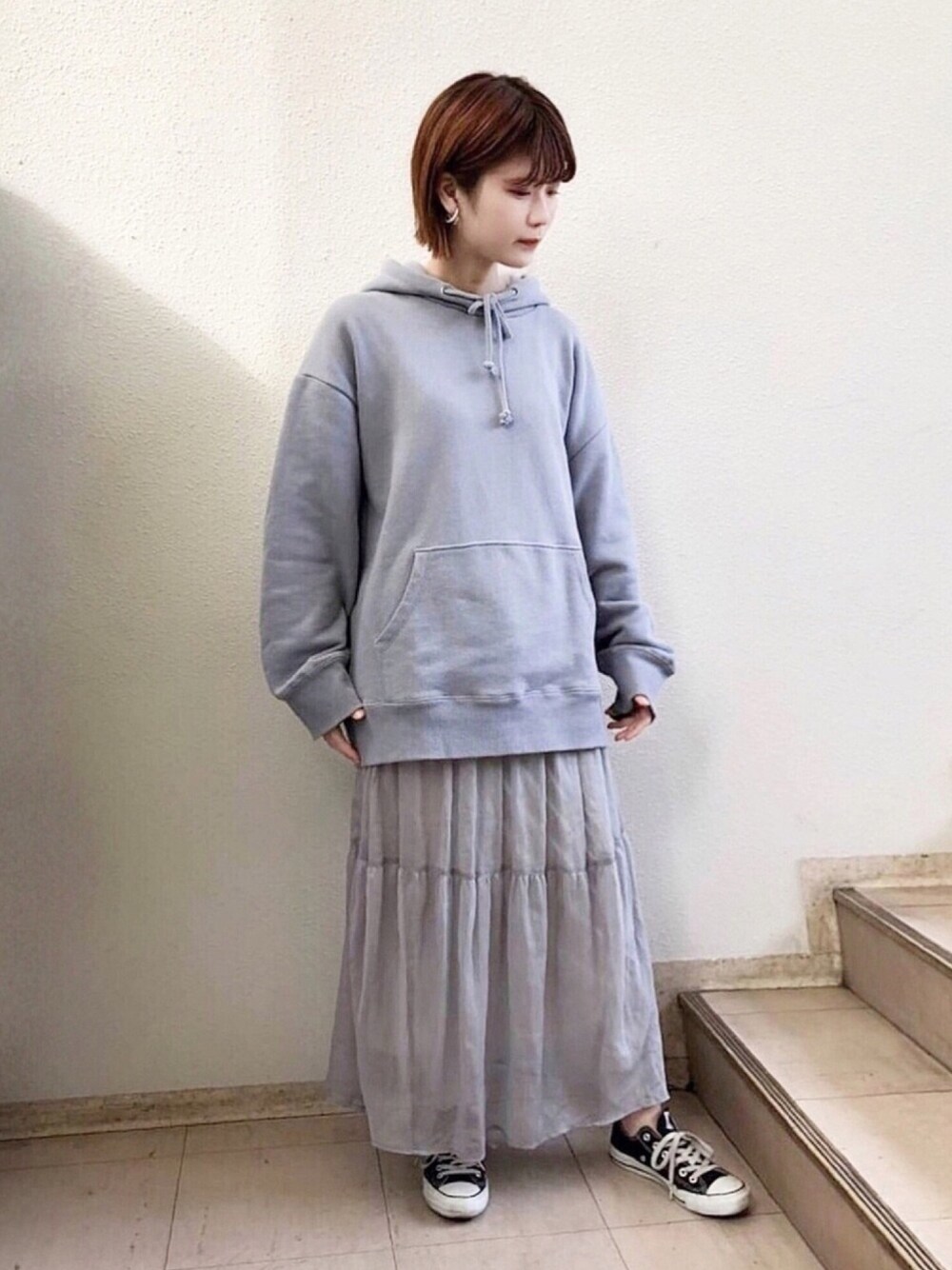 ブルー系のパーカー、グレー系のスカート、ブラック系のスニーカーを着用したレディースの秋コーディネートの1枚目の写真