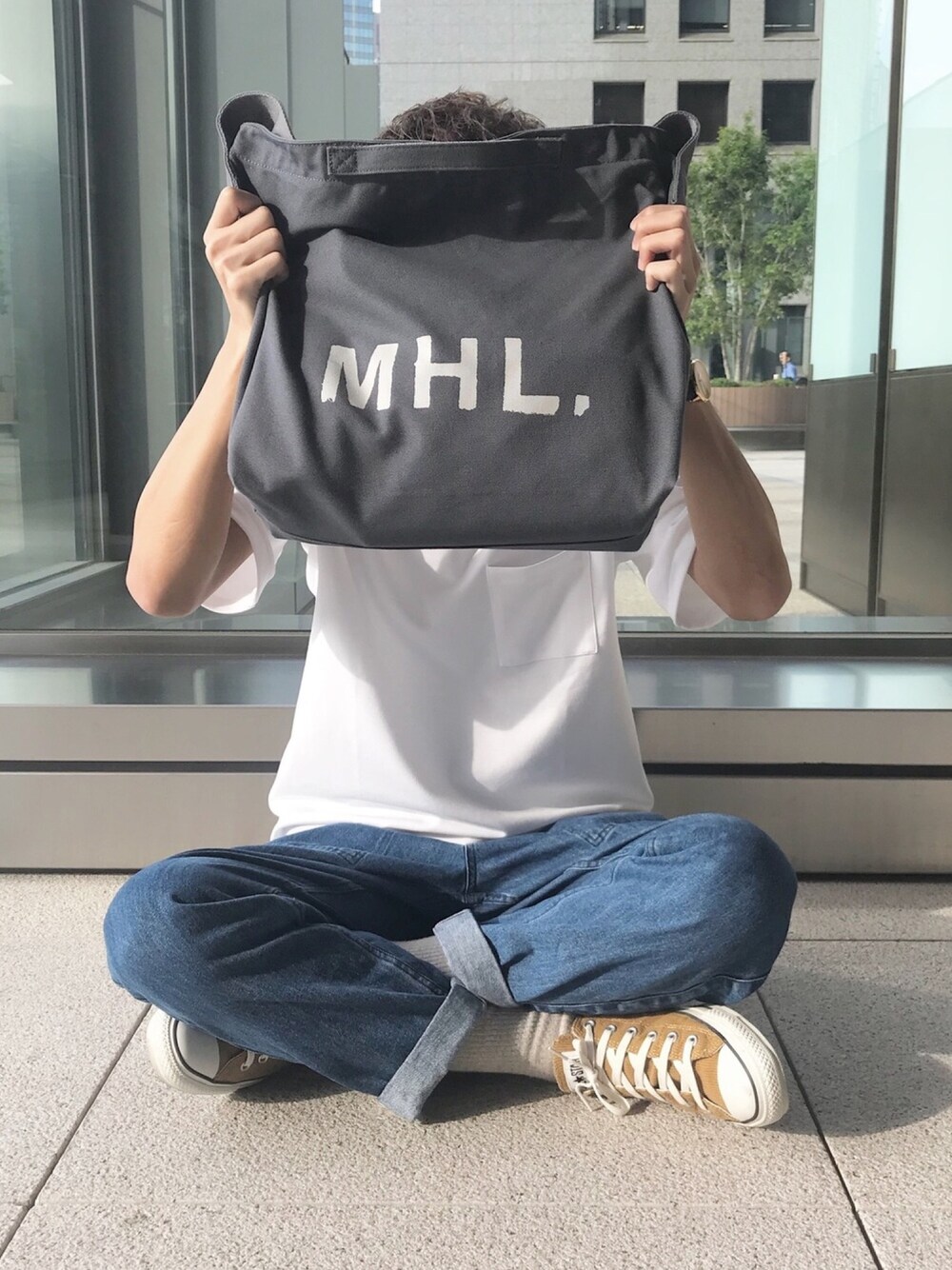 グレー系のトートバッグ、ホワイト系のTシャツ/カットソー、ブルー系のデニムパンツを着用したメンズの夏コーディネートの1枚目の写真