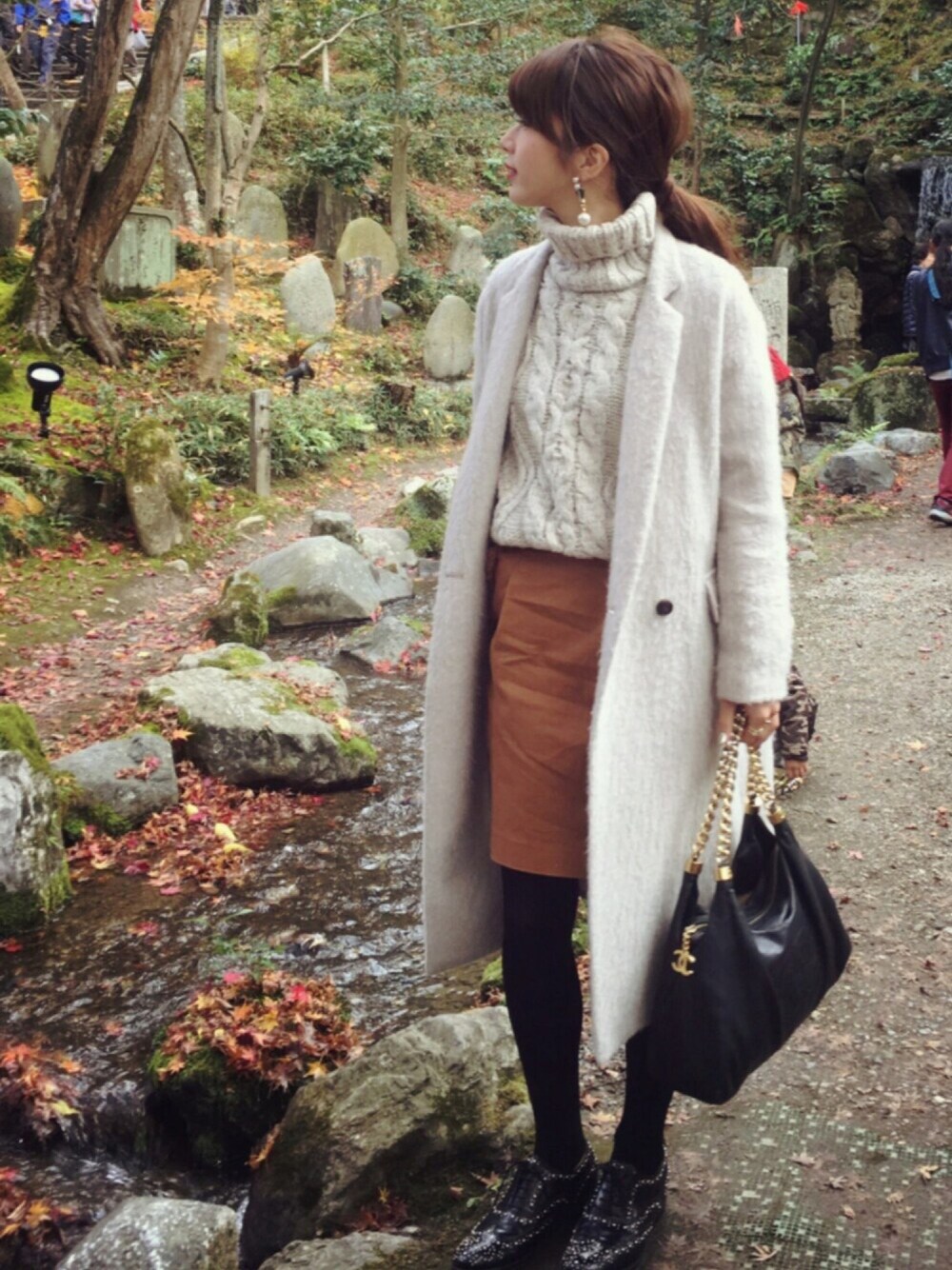 グレー系のチェスターコート、レッド系のスカート、ブラック系のその他シューズを着用したレディースの冬コーディネートの1枚目の写真