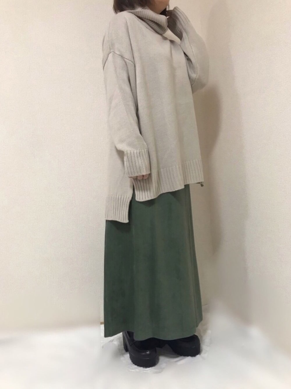 ベージュ系のニット/セーター、グリーン系のスカート、ブラック系のブーツを着用したレディースの冬コーディネートの1枚目の写真