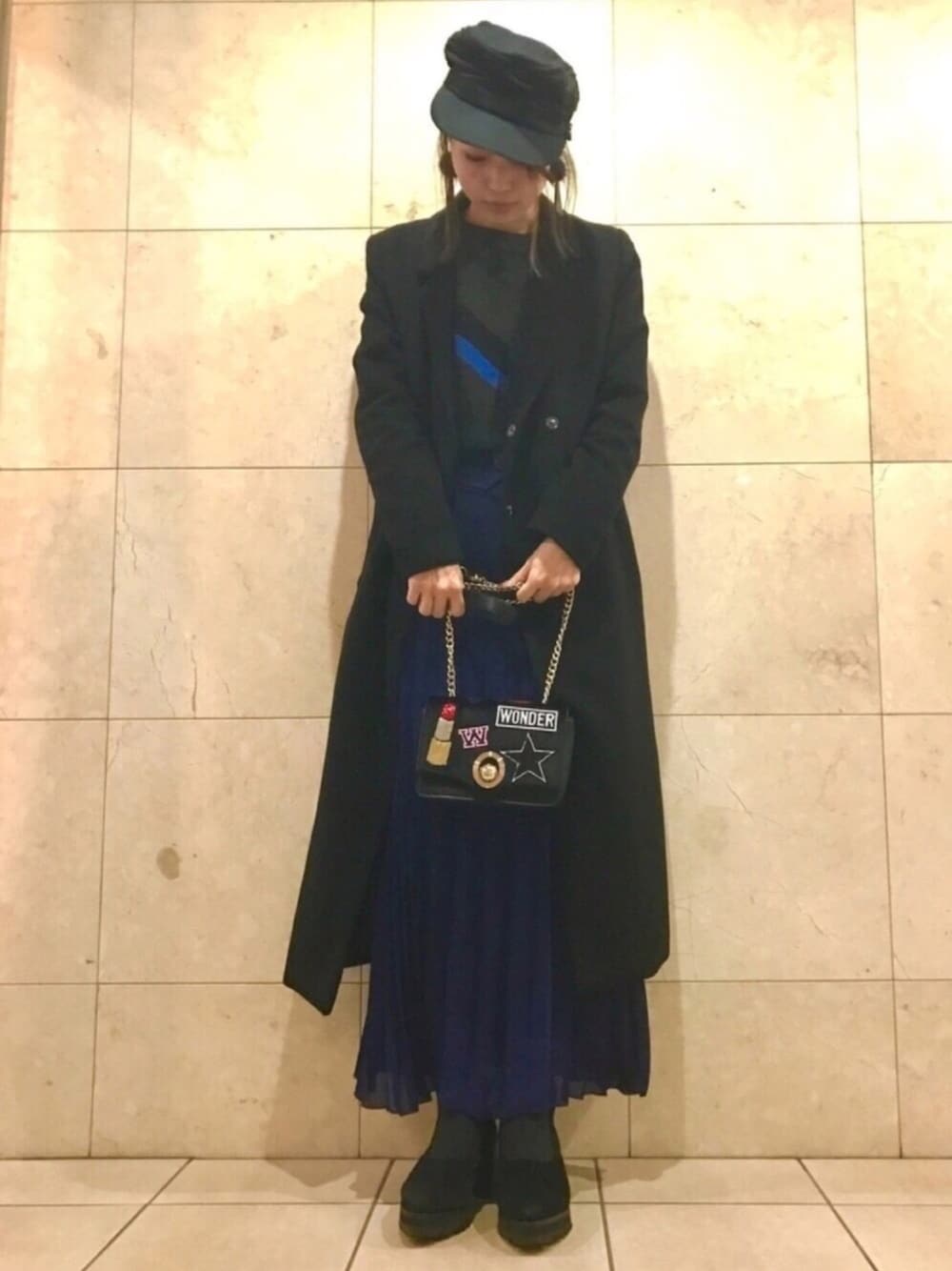 ブルー系のスカート、ブラック系のブーティ、ブラック系のチェスターコートを着用したレディースの冬コーディネートの1枚目の写真