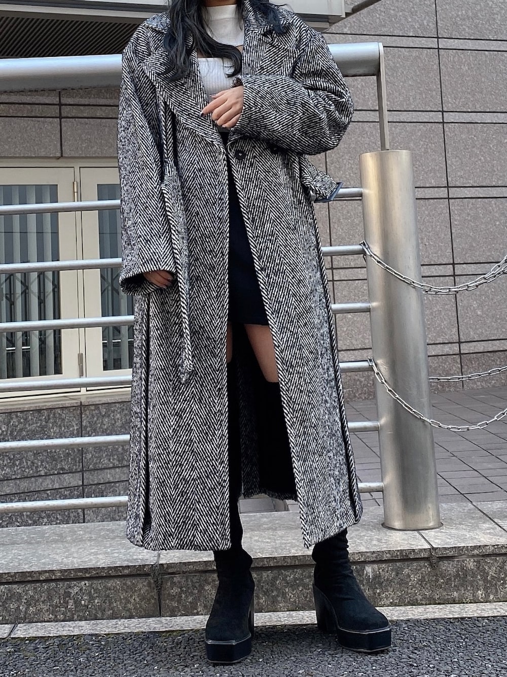 ブラック系のチェスターコート、ホワイト系のニット/セーター、ブラック系のスカートを着用したレディースの冬コーディネートの1枚目の写真