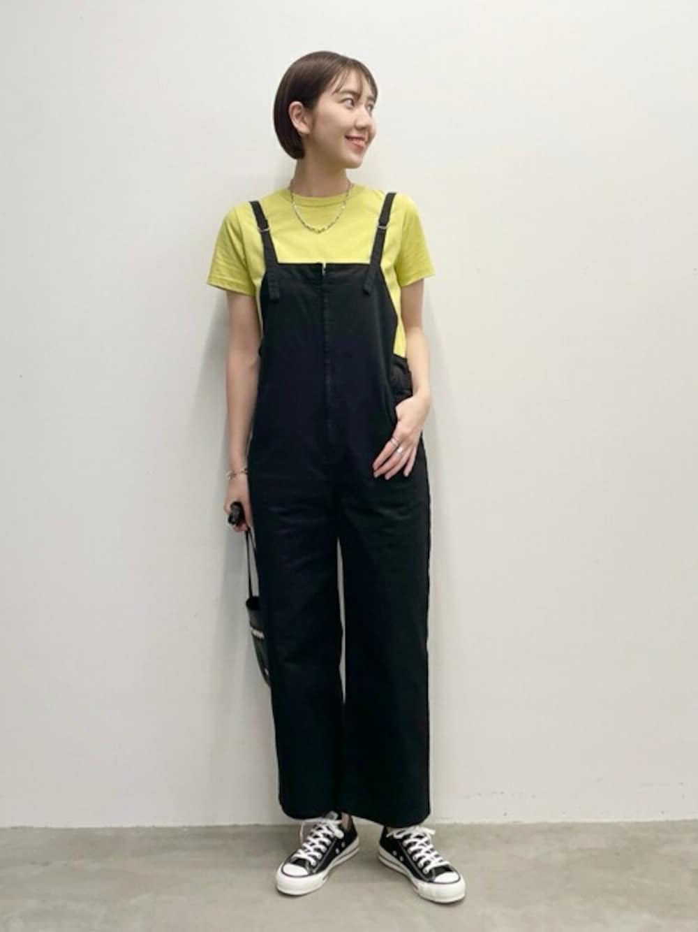 イエロー系のTシャツ/カットソー、ブラック系のサロペット/オーバーオール、ブラック系のスニーカーを着用したレディースの春コーディネートの1枚目の写真