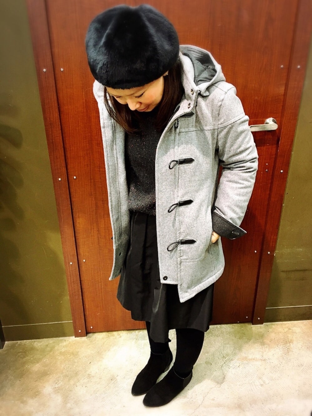 グレー系のダッフルコート、グレー系のニット/セーター、ブラック系のスカートを着用したレディースの冬コーディネートの1枚目の写真
