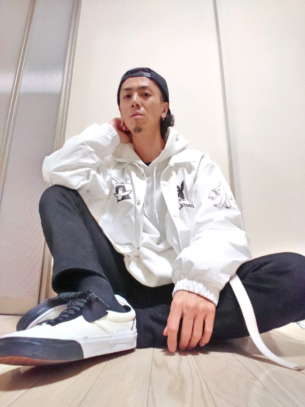 ホワイト系のパーカー、ホワイト系のナイロンジャケット、ブラック系のデニムパンツを着用したメンズの春コーディネートの1枚目の写真