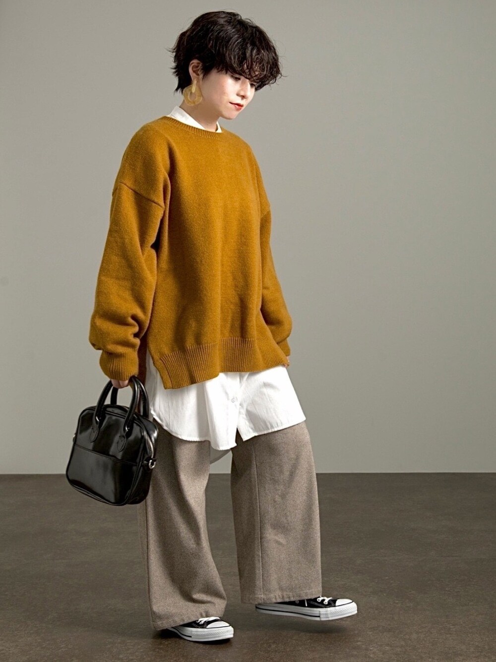 イエロー系のニット/セーター、ホワイト系のシャツ/ブラウス、ブラック系のスニーカーを着用したレディースの冬コーディネートの1枚目の写真