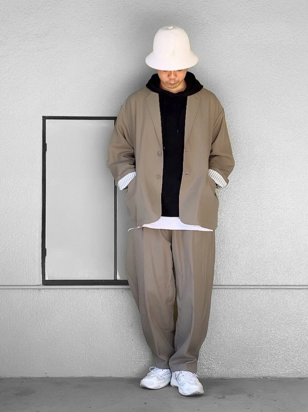 ベージュ系のテーラードジャケット、ホワイト系のスニーカー、ホワイト系のハットを着用したメンズの秋コーディネートの1枚目の写真
