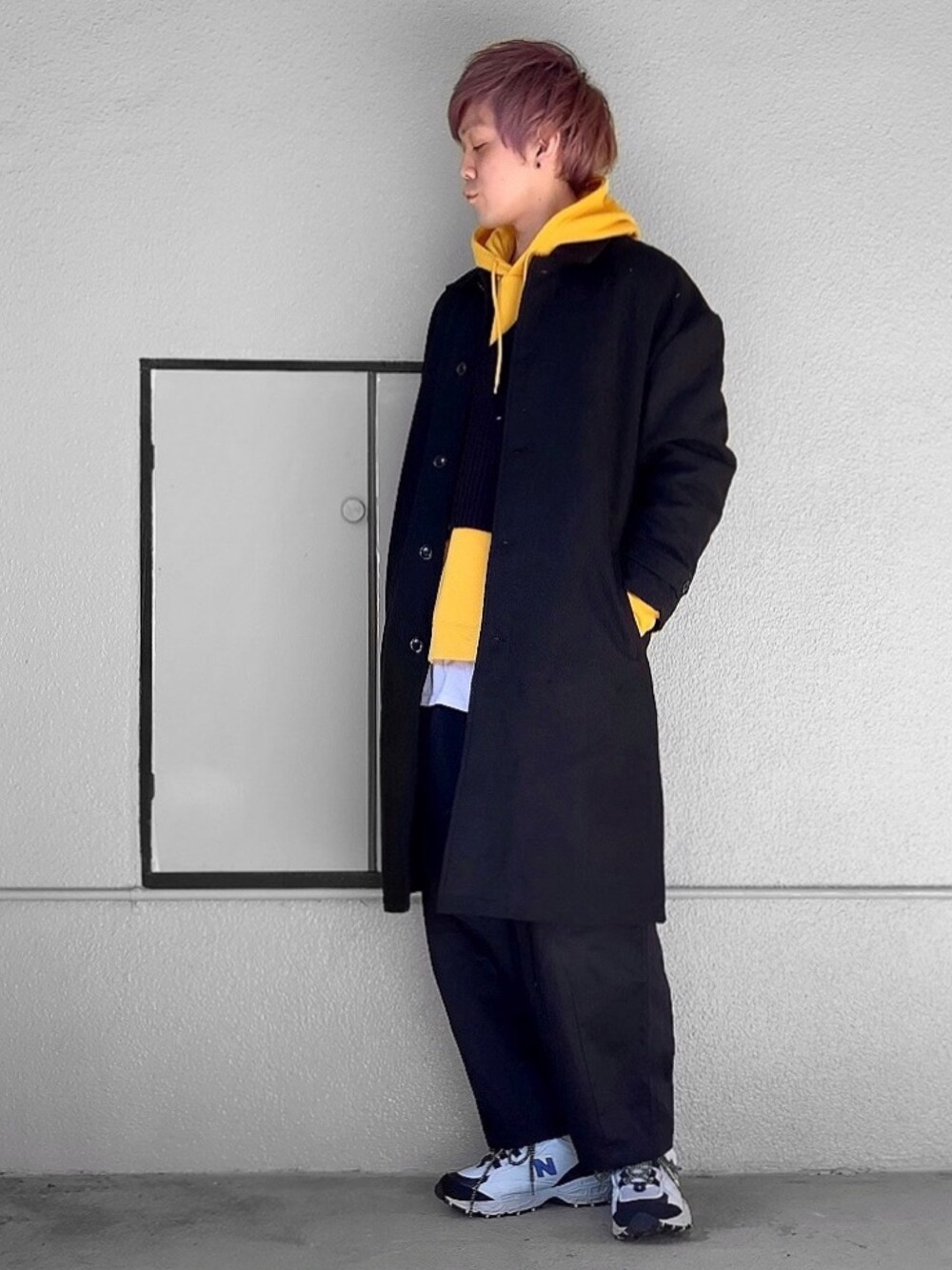 ブラック系のステンカラーコート、イエロー系のパーカー、ブラック系のベストを着用したメンズの冬コーディネートの1枚目の写真
