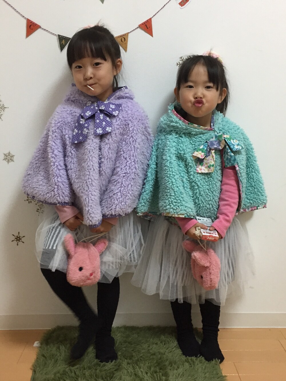 パープル系のポンチョ、グリーン系のポンチョ、ホワイト系のスカートを着用したキッズの冬コーディネートの1枚目の写真