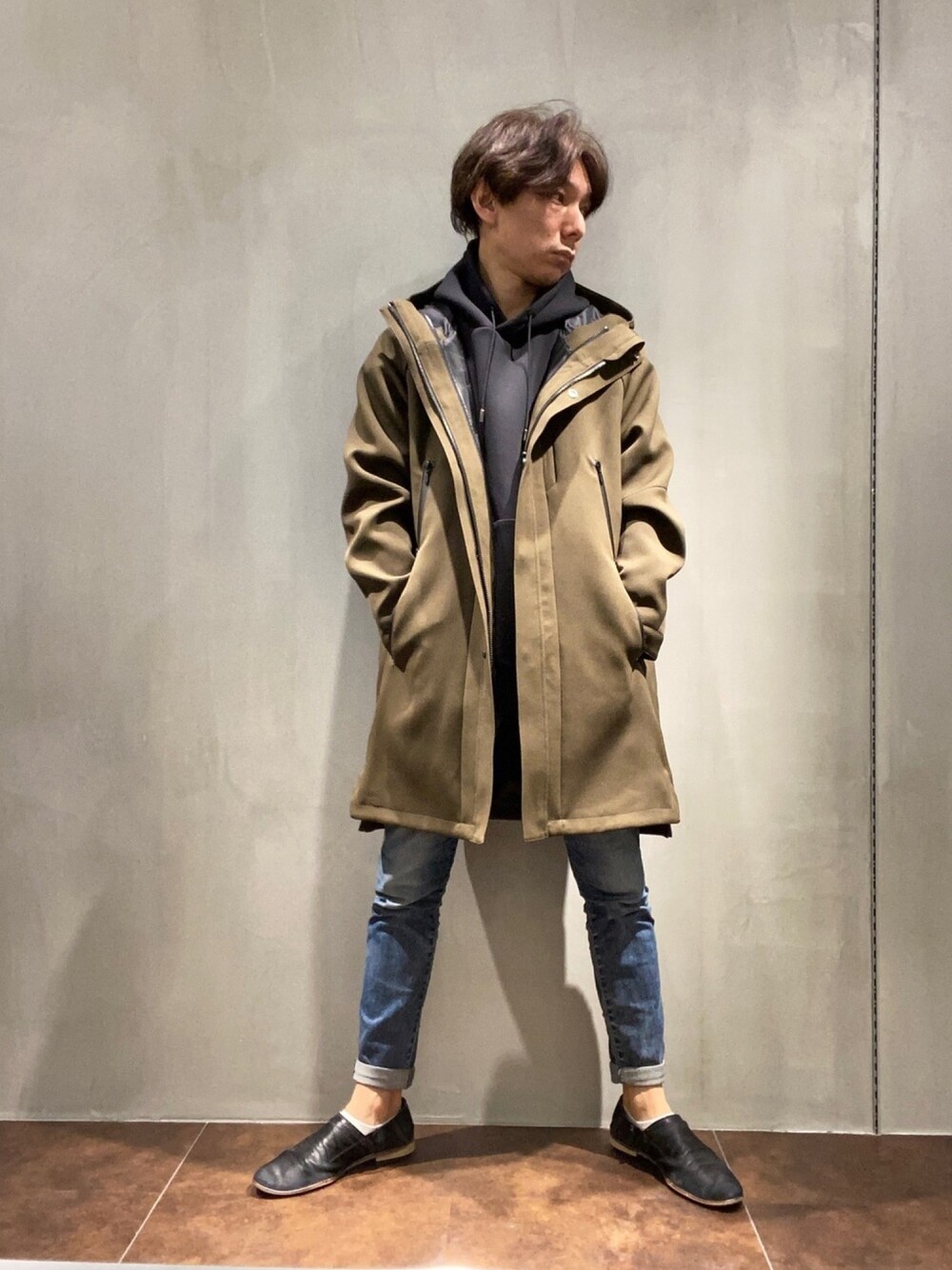 ブラック系のスリッポン、グリーン系のステンカラーコート、ブラック系のTシャツ/カットソーを着用したメンズの冬コーディネートの1枚目の写真