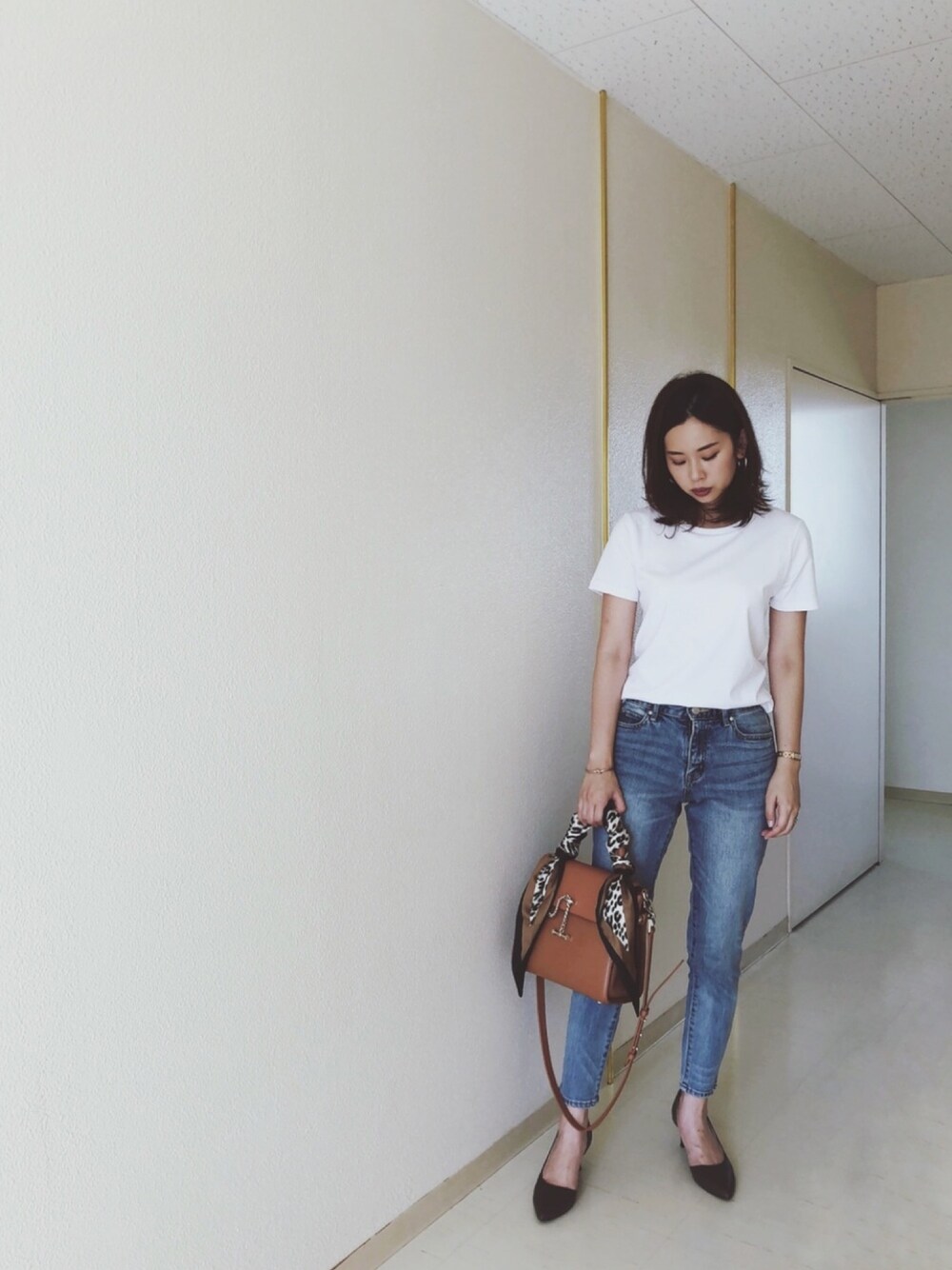 ホワイト系のTシャツ/カットソー、ブルー系のデニムパンツ、ベージュ系のハンドバッグを着用したレディースの秋コーディネートの1枚目の写真