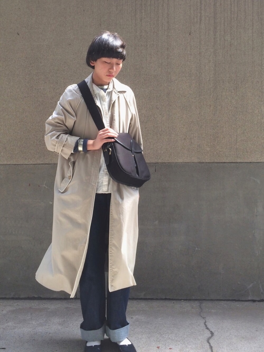 ブラック系のショルダーバッグ、ブルー系のデニムパンツ、ベージュ系のトレンチコートを着用したレディースの春コーディネートの1枚目の写真
