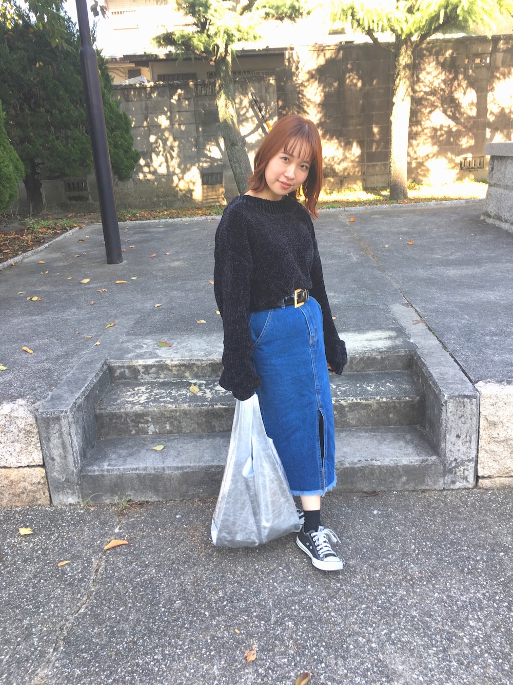 ブルー系のデニムスカート、ブラック系のニット/セーター、シルバー系のトートバッグを着用したレディースの秋コーディネートの1枚目の写真