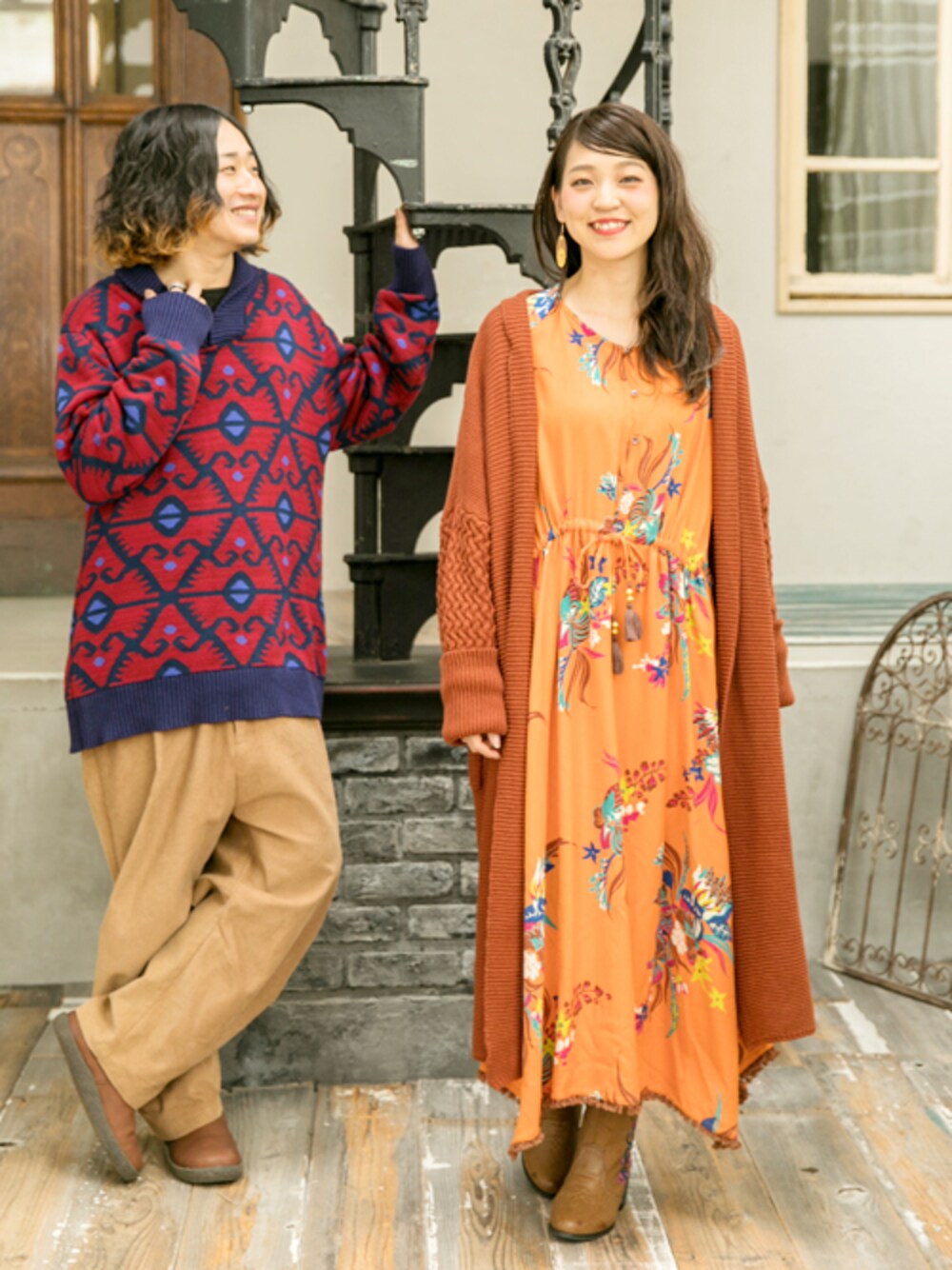 レッド系のカーディガン/ボレロ、オレンジ系のワンピース、ベージュ系のブーツを着用したレディースの秋コーディネートの1枚目の写真