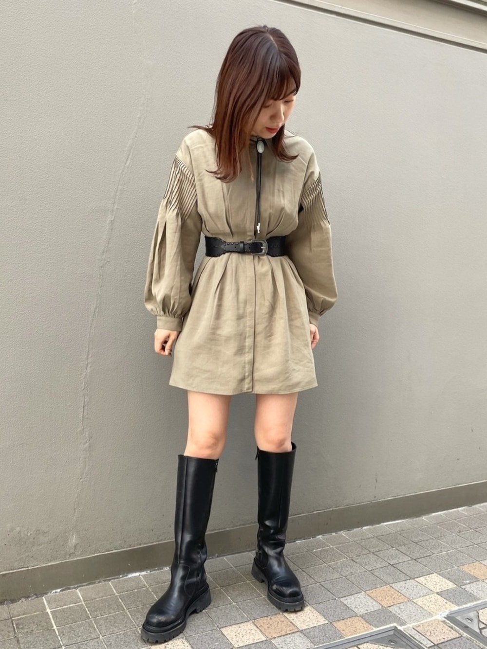 グリーン系のワンピース、ブラック系のブーツ、ブラック系のベルトを着用したレディースの春コーディネートの1枚目の写真