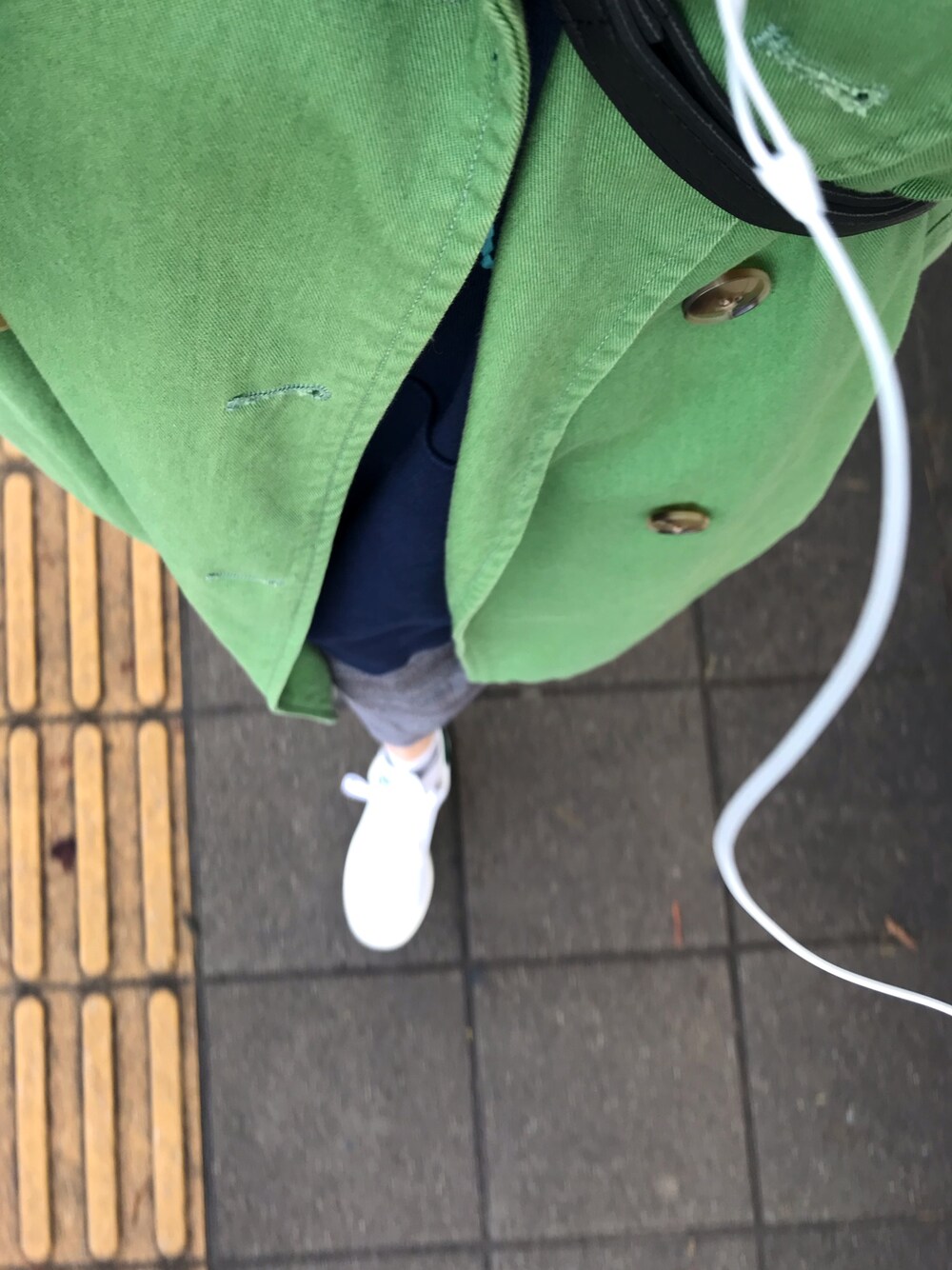 グリーン系のトレンチコート、グレー系のスカート、ホワイト系のスニーカーを着用したレディースの冬コーディネートの1枚目の写真