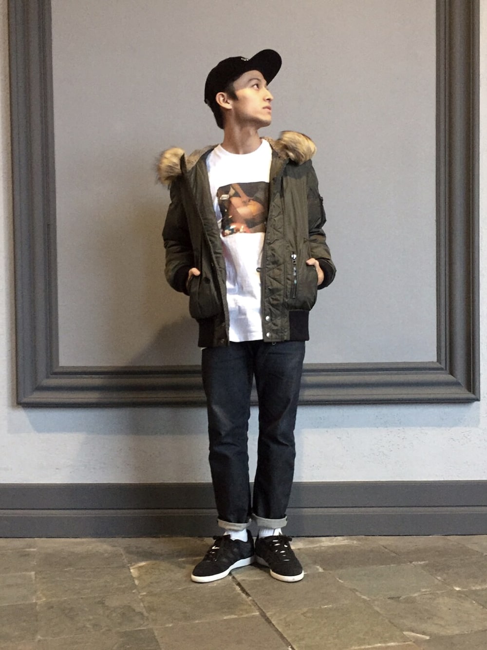 ホワイト系のTシャツ/カットソー、グリーン系のミリタリージャケット、ブラック系のデニムパンツを着用したメンズの冬コーディネートの1枚目の写真