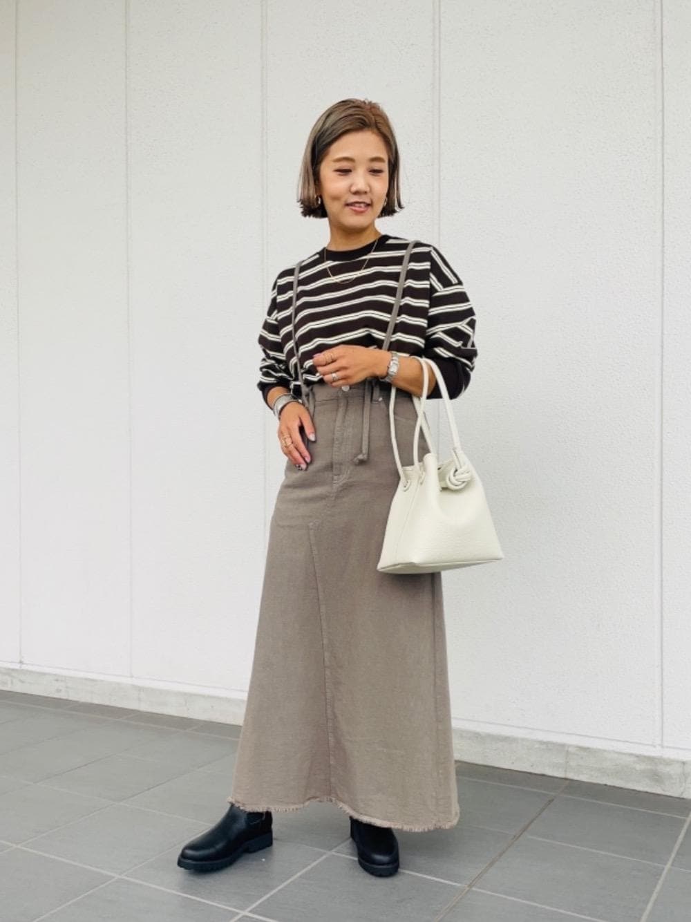 グレー系のデニムスカート、ブラウン系のTシャツ/カットソー、ブラック系のブーツを着用したレディースの夏コーディネートの1枚目の写真