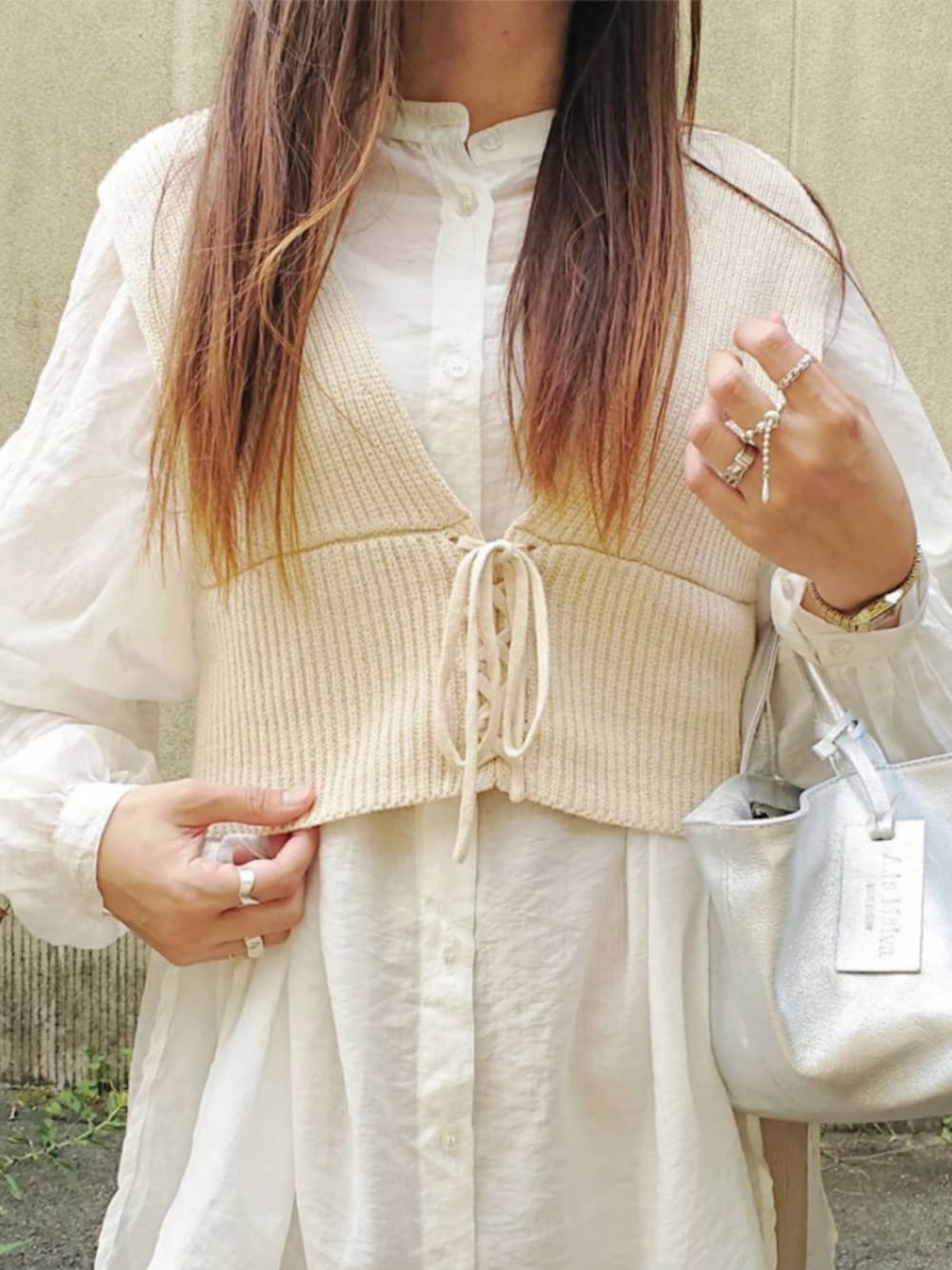 ベージュ系のベスト、シルバー系のバッグを着用したレディースの秋コーディネートの1枚目の写真