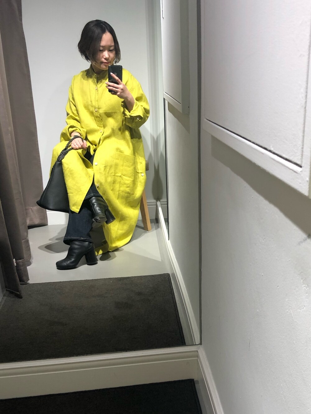 イエロー系のシャツワンピース、ブラック系のハンドバッグ、ブラック系のブーツを着用したレディースの春コーディネートの1枚目の写真