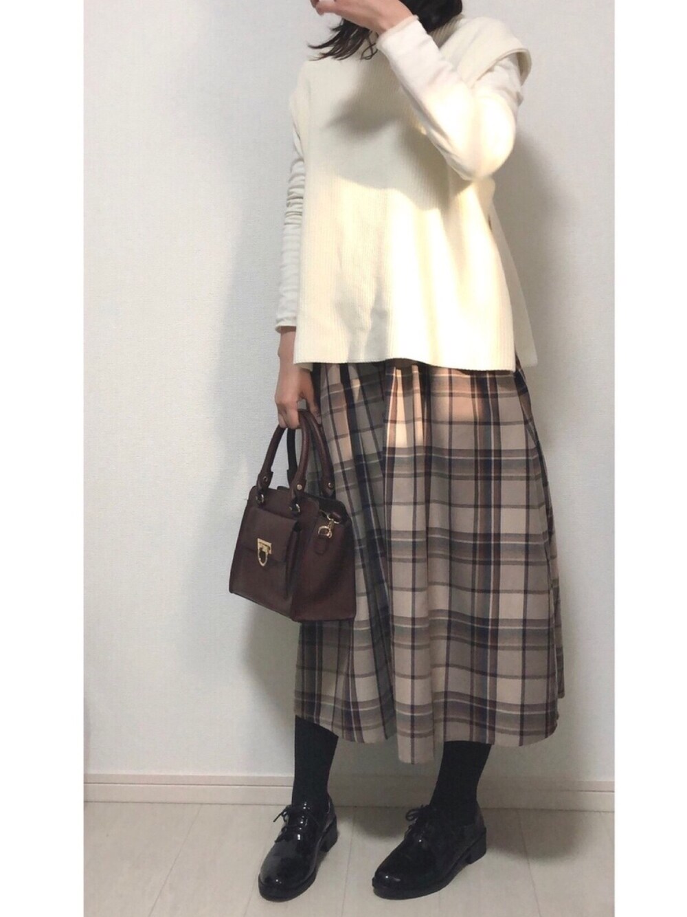 ベージュ系のスカート、ホワイト系のニット/セーター、ブラウン系のハンドバッグを着用したレディースの春コーディネートの1枚目の写真