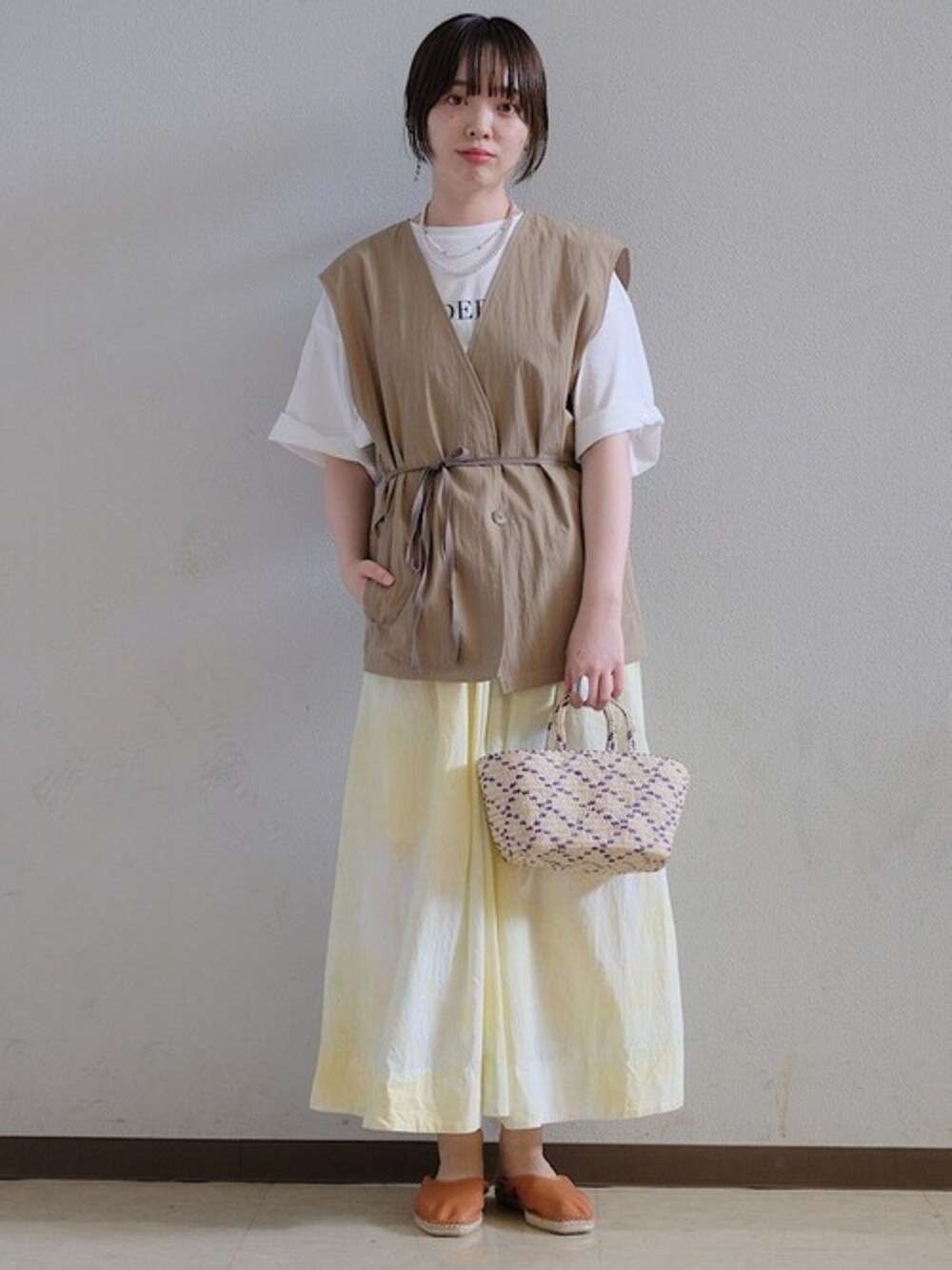 グリーン系のスカート、グリーン系のベスト、ホワイト系のTシャツ/カットソーを着用したレディースの夏コーディネートの1枚目の写真