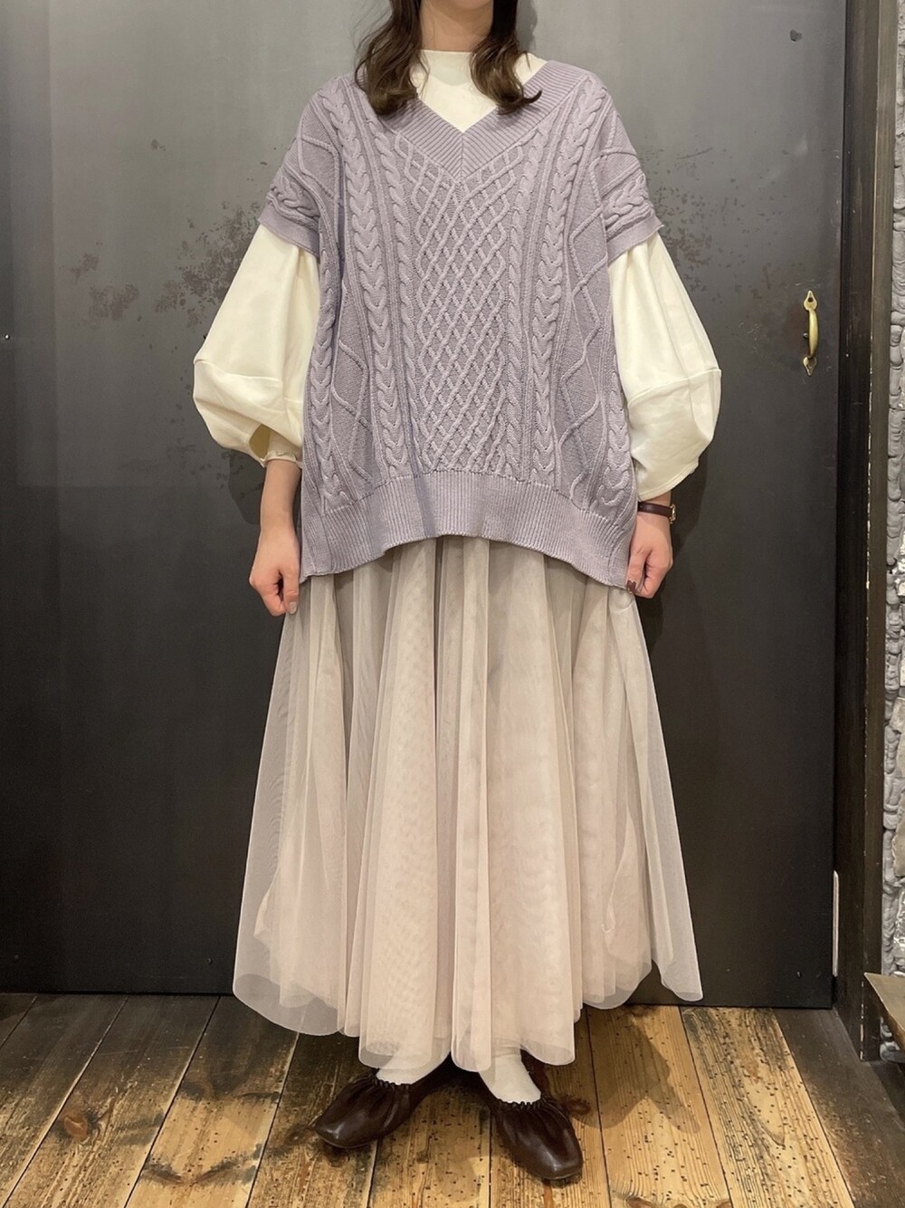 パープル系のベスト、グレー系のスカートを着用したレディースの冬コーディネートの1枚目の写真