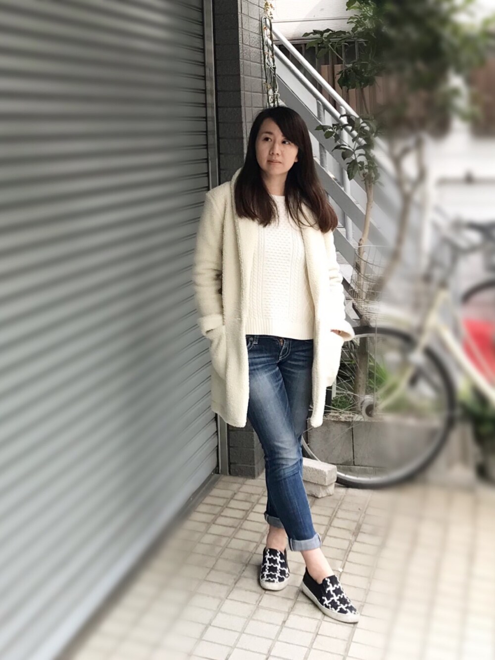 ブルー系のベスト、ブルー系のデニムパンツ、ブラック系のスリッポンを着用したレディースの春コーディネートの1枚目の写真