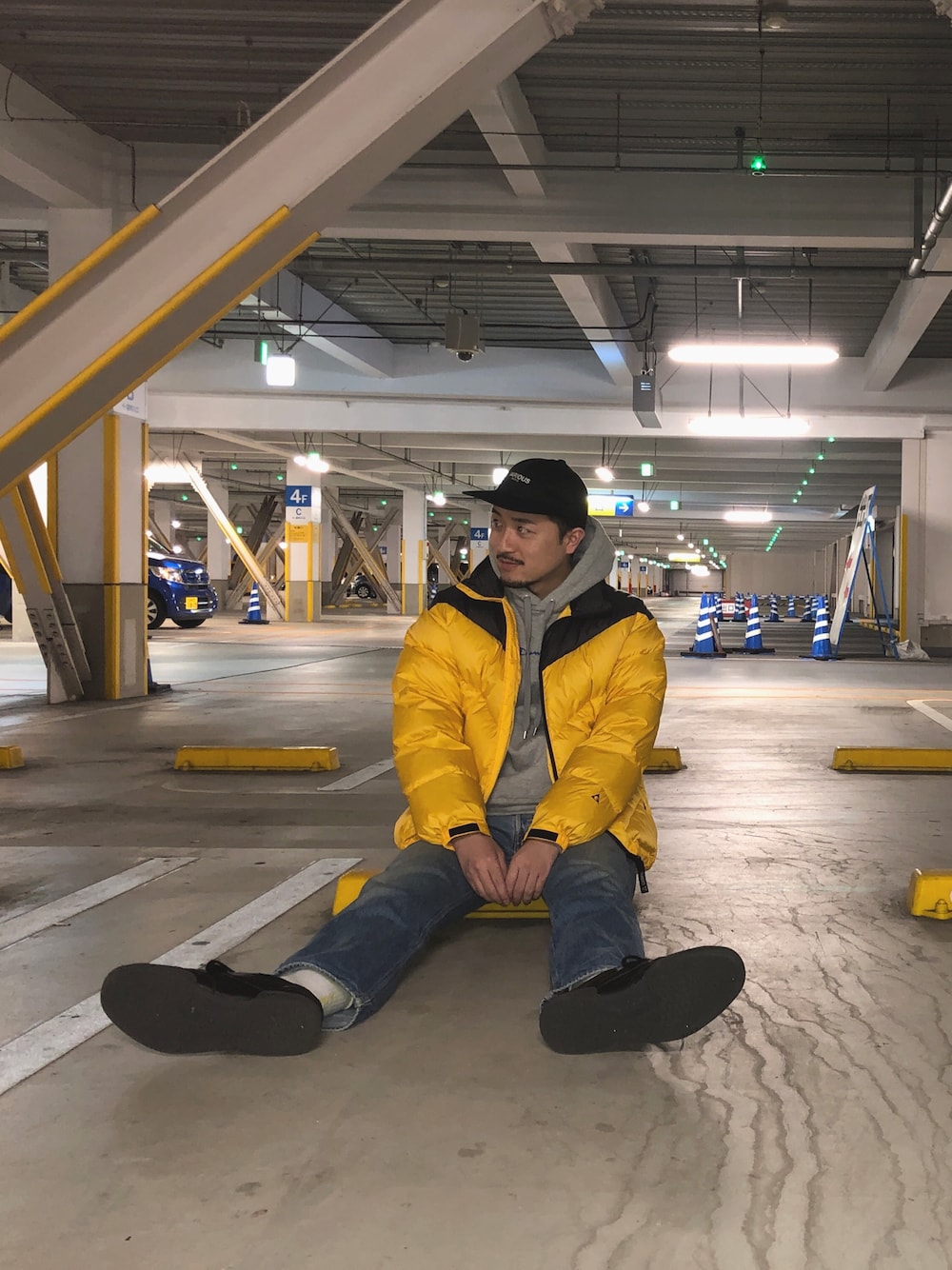 イエロー系のダウンジャケット/コート、グレー系のパーカー、ブルー系のデニムパンツを着用したメンズの秋コーディネートの1枚目の写真