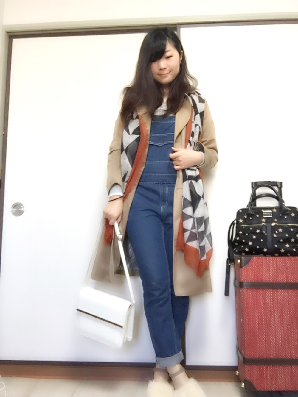 ベージュ系のトレンチコート、ブルー系のサロペット/オーバーオール、ホワイト系のショルダーバッグを着用したレディースの冬コーディネートの1枚目の写真