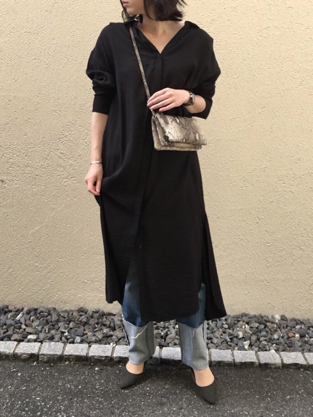 ブラック系のシャツワンピース、ベージュ系のショルダーバッグ、ブルー系のデニムパンツを着用したレディースの夏コーディネートの1枚目の写真